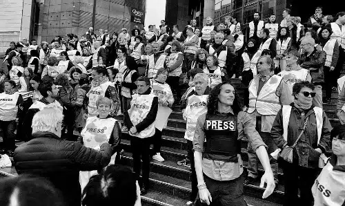 Rassemblement de journalistes en gilet marqué « PRESS » sur les marches d’un bâtiment, en hommage aux reporters palestiniens tués à Gaza et pour dénoncer la répression médiatique.