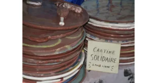 Piles d’assiettes en céramique colorée avec un panneau manuscrit « Cantine solidaire à prix libre », symbole de convivialité et de partage à Uzerche.