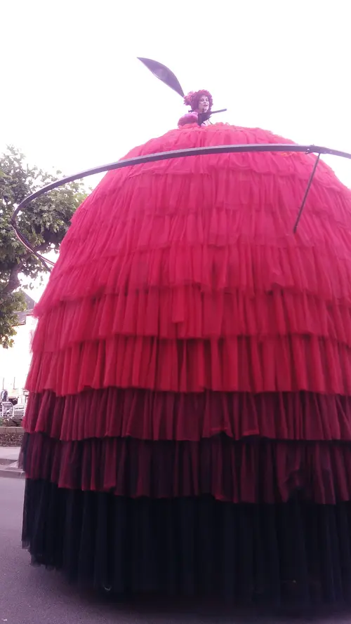 Spectacle de rue à Tulle pendant le festival Tulle remet le son, avec une grande silhouette rouge et noire sur roulettes, coiffée d’une artiste visible au sommet.