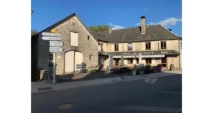 Façade de l'Hôtel de la Poste à Saint-Privat, bar-restaurant de village en pierre avec terrasse fleurie, panneaux directionnels et ciel bleu.