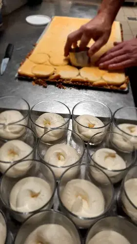 Préparation de desserts à l'Hôtel de la Poste à Saint-Privat – verrines de mousse à la vanille alignées et cuisinier découpant des disques de pâte sur une plaque.