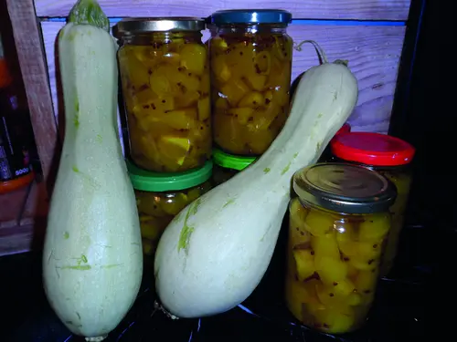Deux courgettes fraîches et des bocaux de courgettes marinées préparés par Paulette.