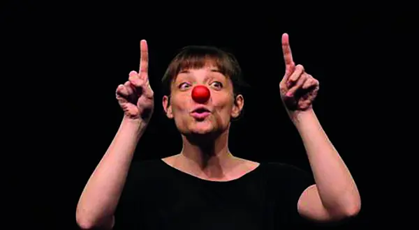 Photo : une femme au nez rouge de clown, deux doigts levés, sur fond noir