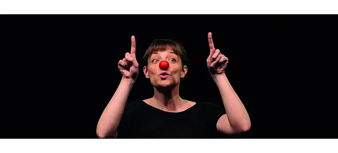 Photo : une femme au nez rouge de clown, deux doigts levés, sur fond noir