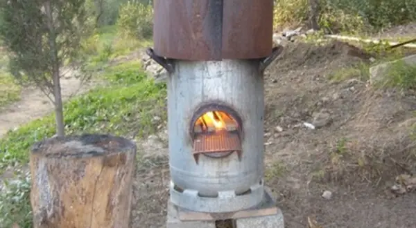 Photo : un rocket stove en tôle, fagots de bois à proximité