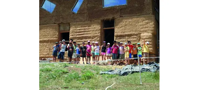 Photographie d’une classe de CM1-CM2 devant une maison en paille, à Saint-Bonnet-l’Enfantier.