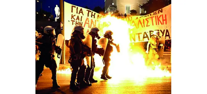 Photographie d’une manifestation en Grèce, avec des fumées et une banderole.
